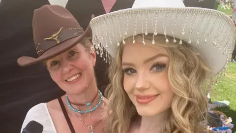 Sara Dunleavy Two women in a selfie picture. They are wearing cowboy hats and outfits. One of them is holding a microphone.
