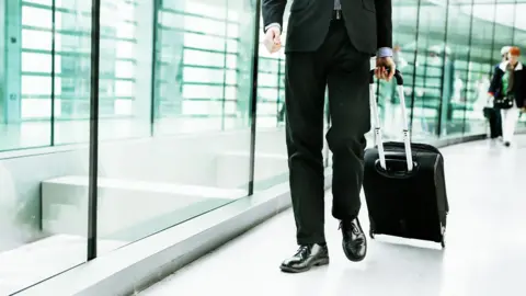 Getty Images/Astrakan Images Businessman walking with luggage at airport (stock photo)