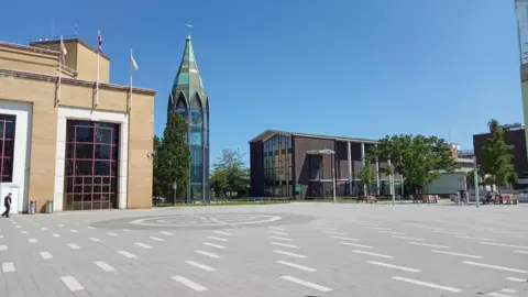 A view of a wide open space with modern budlings around it. A blue sky is above.