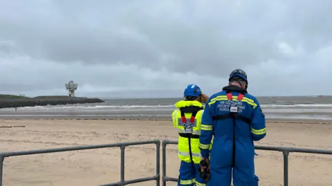 BBC/Leanne Harper Search and rescue workers looking out to sea in search for missing teenager at Crosby Beach