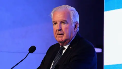 Sir Craig Reedie speaking at a podium in 2018