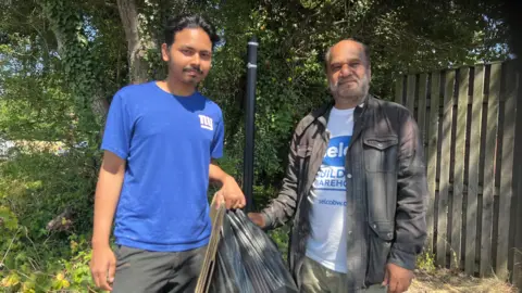 Two men - one is older, one younger. They hold bags of rubbish.