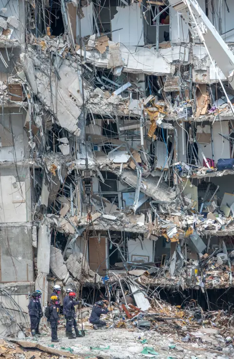 EPA Rescue teams stand amid rubble of collapse building