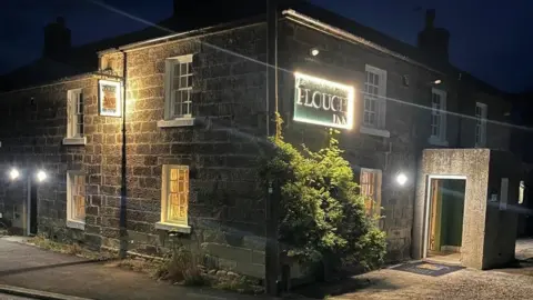 Paul Johnson The image shows a square Georgian building at night with the name, the Plough inn lit up 