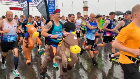 Dozens of runners setting off from the start line of the Plymouth half marathon on the Hoe in the city. Many are wearing fancy dress costumes.