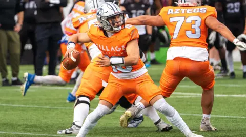 Ben Rogers / BAFA Bristol Aztecs players wearing orange and white uniforms and helmets. A player is facing the camera getting ready to throw the ball.