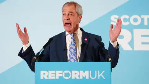 PA Media Reform UK leader Nigel Farage standing behind a podium and in front of a blue wall with the name of the party.