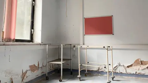 A abandoned clinic is depicted with a red noticeboard and peeled wallpaper