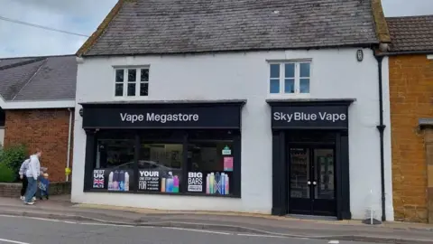 A white terraced house with black doors and frontage with "Vape Megastore" and "Sky Blue Vape" written on it. 