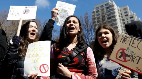 Reuters Three students hold various signs in New York City school walkout