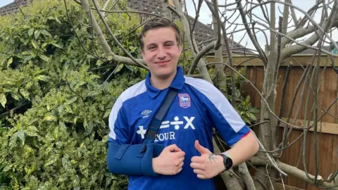 Rémi Mills Rémi Mills poses with his shoulder bandage after dislocating his shoulder at an Ipswich Town game