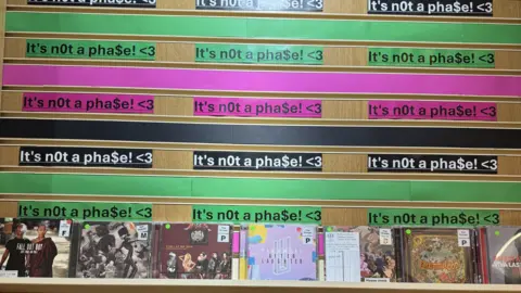 Museum of Youth Culture A CD stand with the phrase "It's not a phase" written above multiple times.
