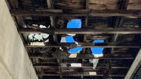 Canopy above the Scott Cinema building with holes in it. There is a man walking along the pavement and there are buildings in the background.