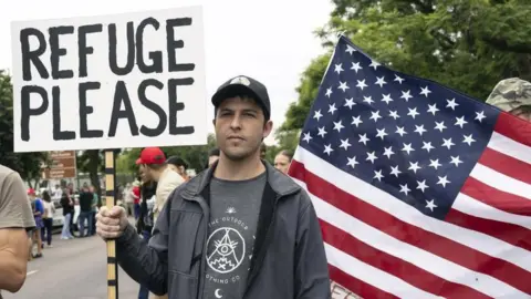 EPA Afrikaans farmer wearing a cap and black jacket, holding a placard written "Refuge Please" behind a US flag 