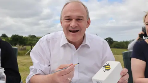 Liberal Democrats Liberal Democrat leader Sir Ed Davey holding a paintbrush in the one hand and in the other a pot with a bee painted on the side.