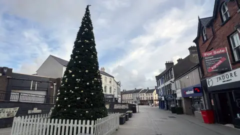 An artificial tree is placed in the centre of a street in Carrickfergus. The bottom of the tree is fenced off with a white picket fence and there are a number of silver baubles on it.