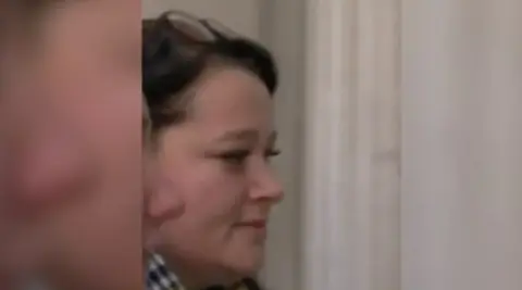 A close-up photograph of Melissa Wilband's face as she enters court. She is in her late 20s and has glasses on top of her head. The nose of a woman walking next to her can be seen.