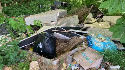 BBC/Simon Thake Old beds, mattress, bin bags and dirty shopping bags are scattered amongst shrubs