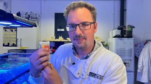 Professor Michael Sweet holds a tube of the new coral-friendly sunscreen