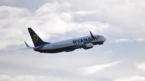 A Ryanair aeroplane mid flight against a cloudy sky.