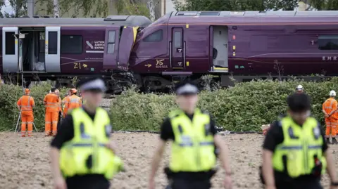 EPA/Shutterstock Out of focus emergency workers are stood near two crashed trains behind them.