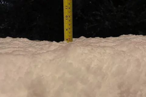 Mark Hatton Thick layer of snow with a tape measure sticking out the top