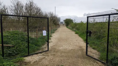 Wandle Valley Forum Two black gates are open with a large gravel path down the midland and greenery on either side. 