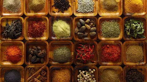 Getty Images A large selection of commonly used Indian cooking spices in wooden trays on an old table.