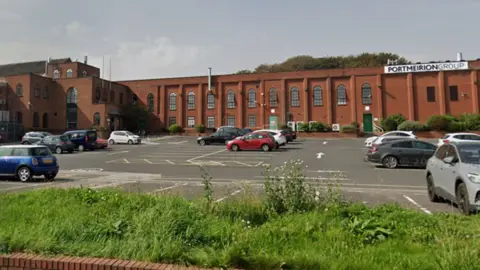 A large red brick factory stands at the back of a large car park. There is a large sign to the right of the building which reads Portmeirion Group.