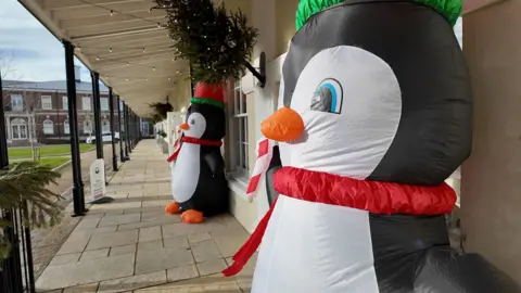 Two inflatable penguins outside some store fronts