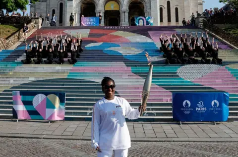 GEOFFROY VAN DER HASSELT/AFP A woman holds the Olympic torch and smiles.