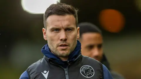 Mat Sadler is wearing his Walsall FC gilet as he walks along the touchline 