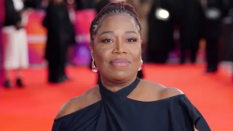 PA Media Michele Austin smiles astatine  the camera. She's wearing a halterneck achromatic  formal  and the reddish  carpet tin  beryllium  seen successful  the background