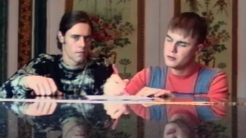Take That/Netflix Howard Donald and Gary Barlow, pictured during the early days of Take That, are pictured sitting at a piano in this candid image. Barlow is making notes on a piece of paper.
