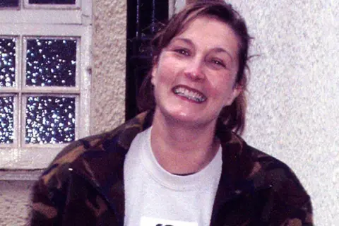 PA Media Suzanne Pilley smiles at the camera. Her brown hair it tied back and she wears a white top and camouflage jacket