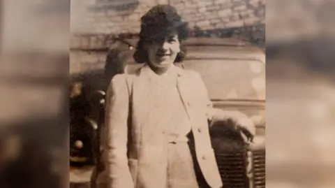 Handout A black and white photo of Joyce in her youth leaning up against the hood of a car wearing a dark hat and blazer