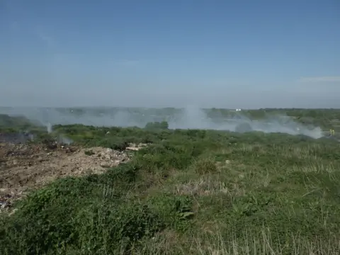 London Fire Brigade. Smoke smoulders in a scrubby field