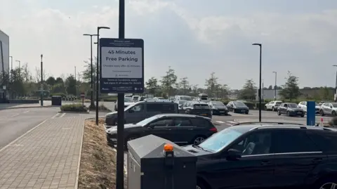 Picture of the car park at Ice Planet. A sign reads 45 minutes free parking. Their are multiple cars parked on site.