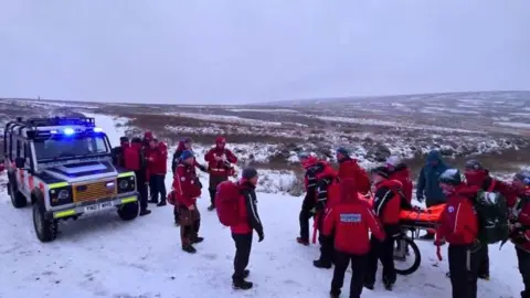 Buxton MRT Un vehículo MRT estacionado en un terreno nevado con varios voluntarios cerca