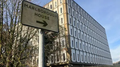 BBC Marlborough House, a large square block building with white circular windows with rectangular glass all on concrete walls.  There is a sign that reads Marlborough House.