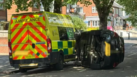 An overturned car next to an ambulance in the aftermath of a collision in Blackbird Road, Leicester.