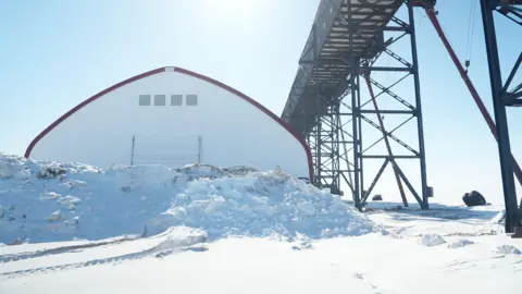 Eloise Alanna/BBC News An image showing the Port of Churchill infrastructure, including a white domed structure and a metal ship loader on the right. In front of the domed structure is a big snow bank.