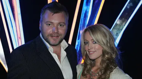 Getty A young man in a suit and a blone-haired woman wearing a silver necklace smile at the camera