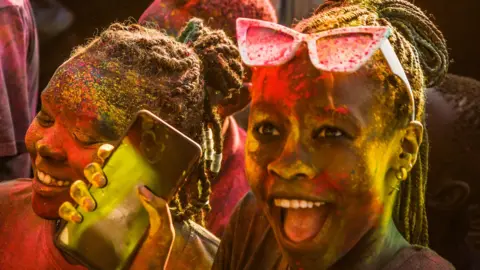 Two girls covered in yellow and pink paint smile.