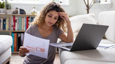 A young woman looks concerned while reading a bill