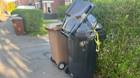 An overflowing black bin. 