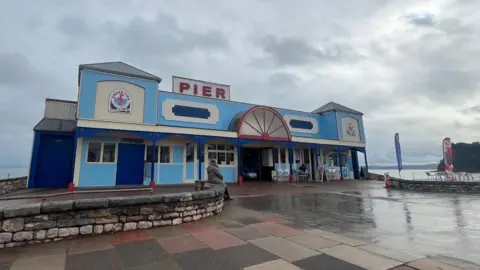 The pier at Teignmouth is a blue and cream building with a red and white sign on the top.