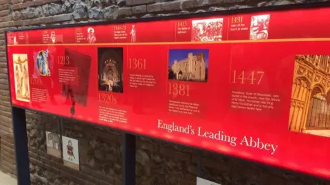 Katy Lewis/BBC The period of time between the 1200s and 1447 can be seen in a section of a timeline in the cathedral's visitor centre. Colour photgraphs and white text are on a red background.