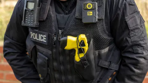 Armed policeman in London showing a Taser in a holster. Stock image.