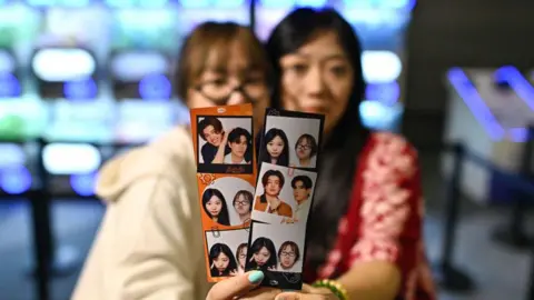 Getty Images This photo taken on April 23, 2024 shows Thai fans hold photographs of popular "Boys' Love" drama actors Naravit "Pond" Lertratkosum and Phuwin Tangsakyuen during a GMMTV promotional event in Bangkok.